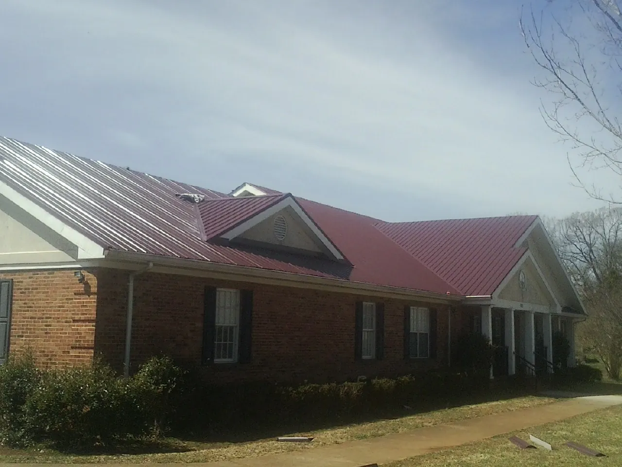 Red metal roof with gabled entries on a long brick building, from a Hail Damage Roof Repair job in Rancho Santa Fe